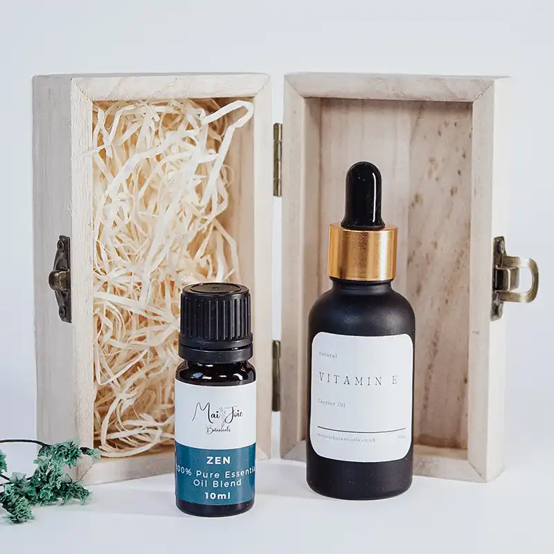 Handcrafted aromatherapy blending kit with a reusable wooden storage box, a sleek black glass dropper bottle of Vitamin E, and a Zen pure essential oil blend